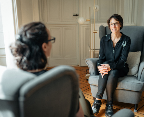 two women sitting in chairs facing each other and talking