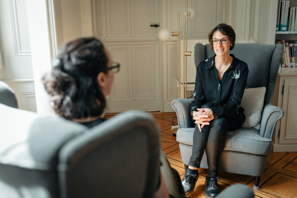 two women sitting in chairs facing each other and talking