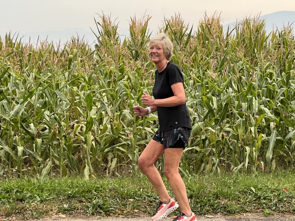 Woman running with corn fields behind her.