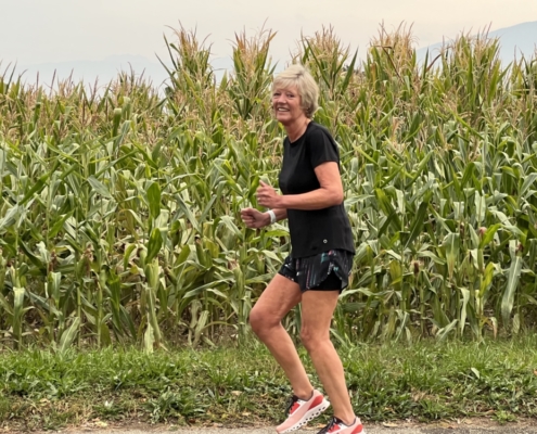 Woman running with corn fields behind her.